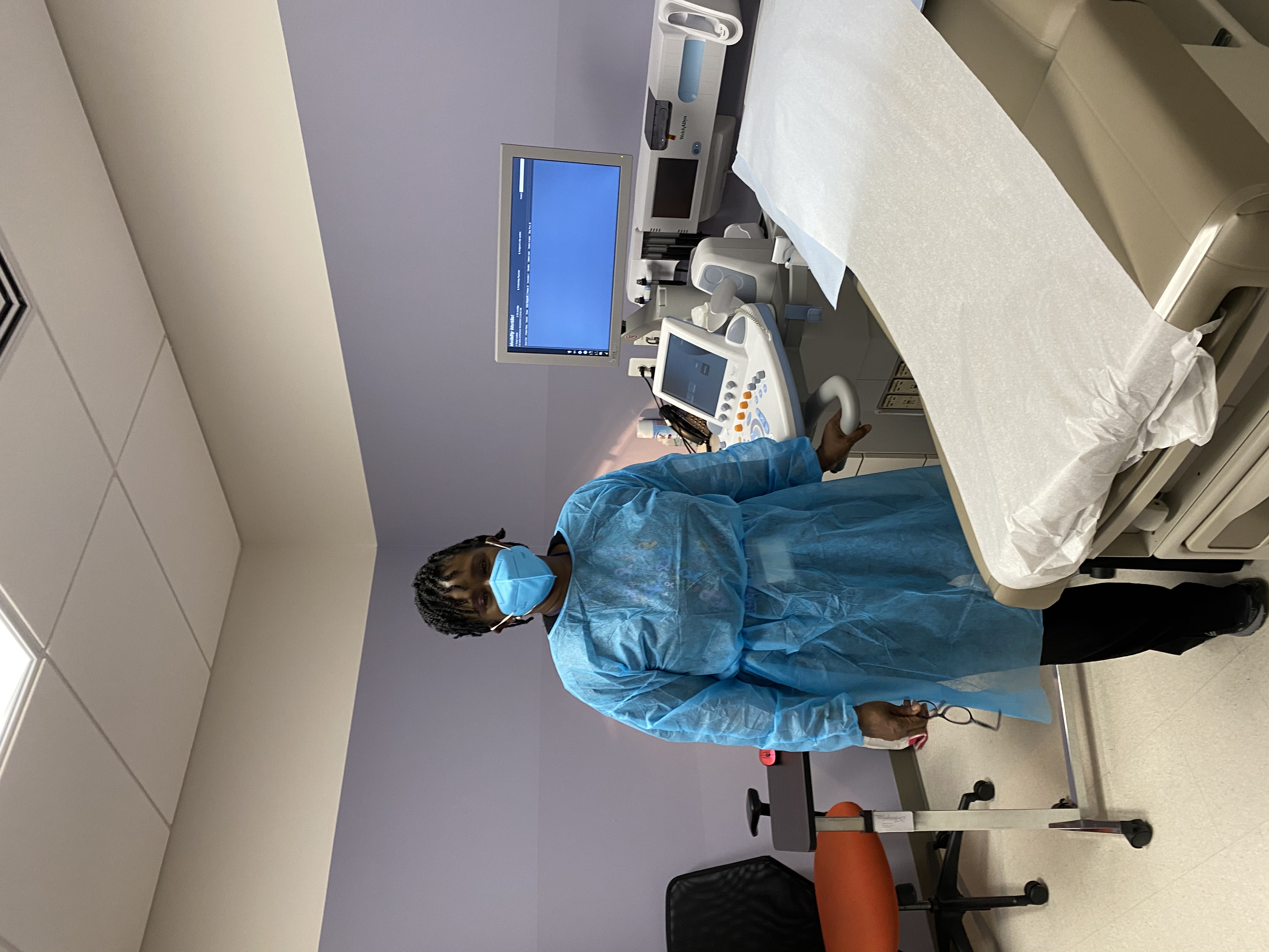 A woman in an exam room wearing a mask and gown