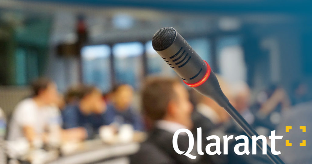 Qlarant logo overlaid on a microphone in a conference room